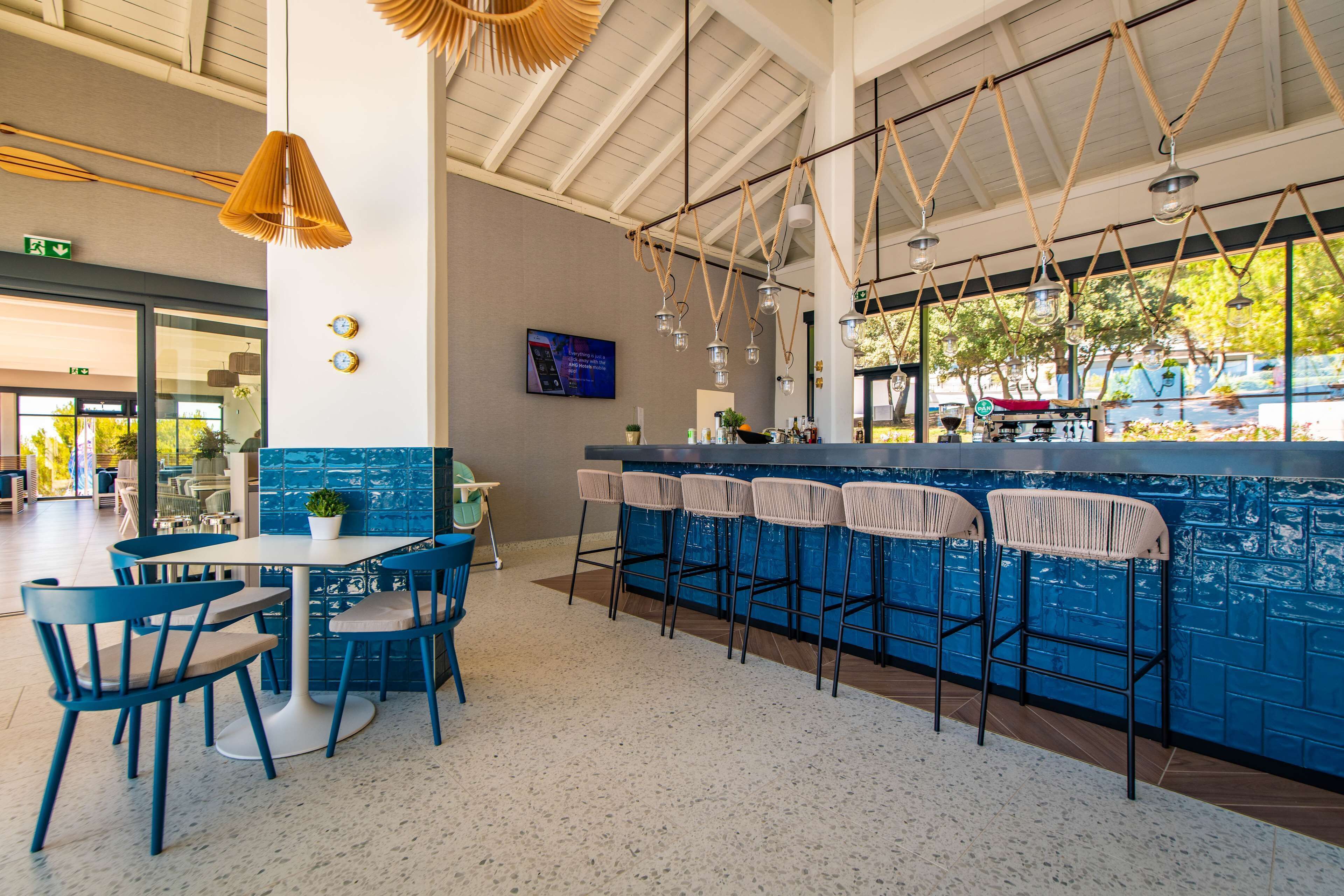 Un espace bar avec des tabourets bleus, une table blanche et des lampes suspendues.