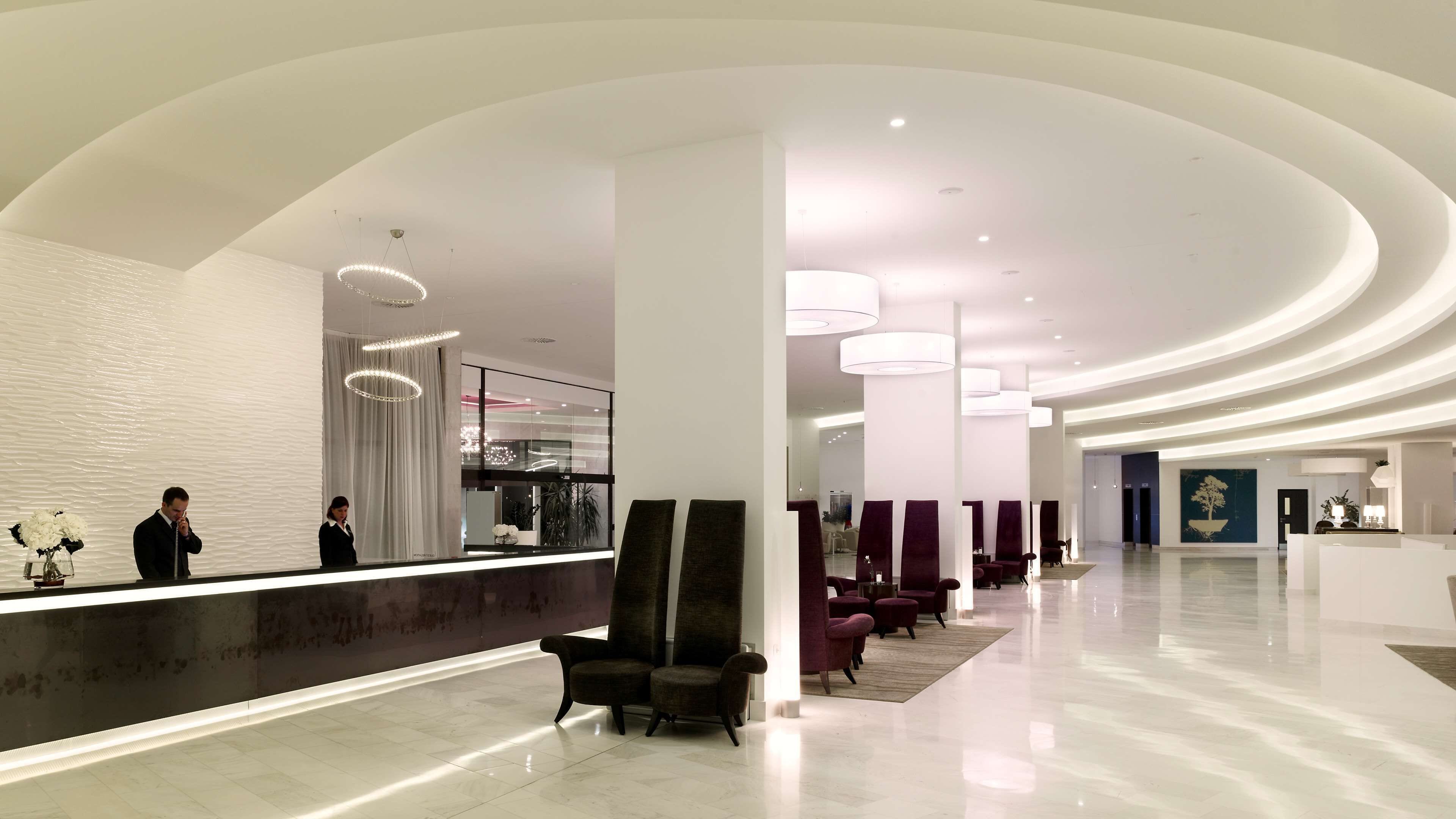 A modern hotel lobby with a reception desk, seating area, and a large window.