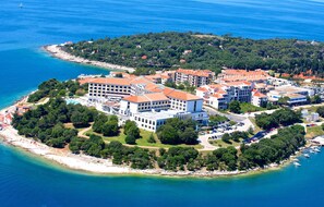 Vista aérea de un hotel costero con varias construcciones, una playa y un puerto deportivo.