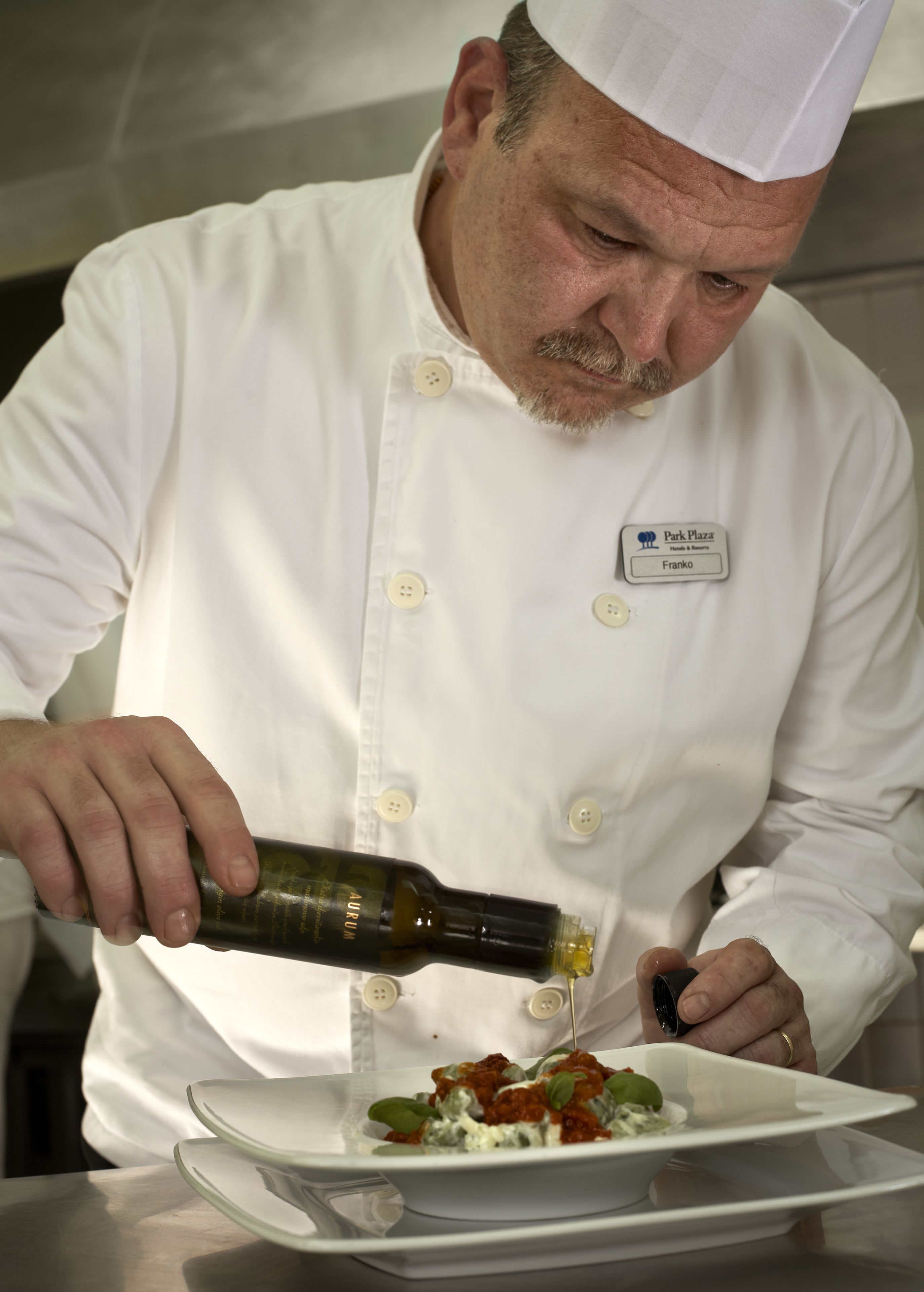 A chef in a white uniform pouring sauce onto a dish.