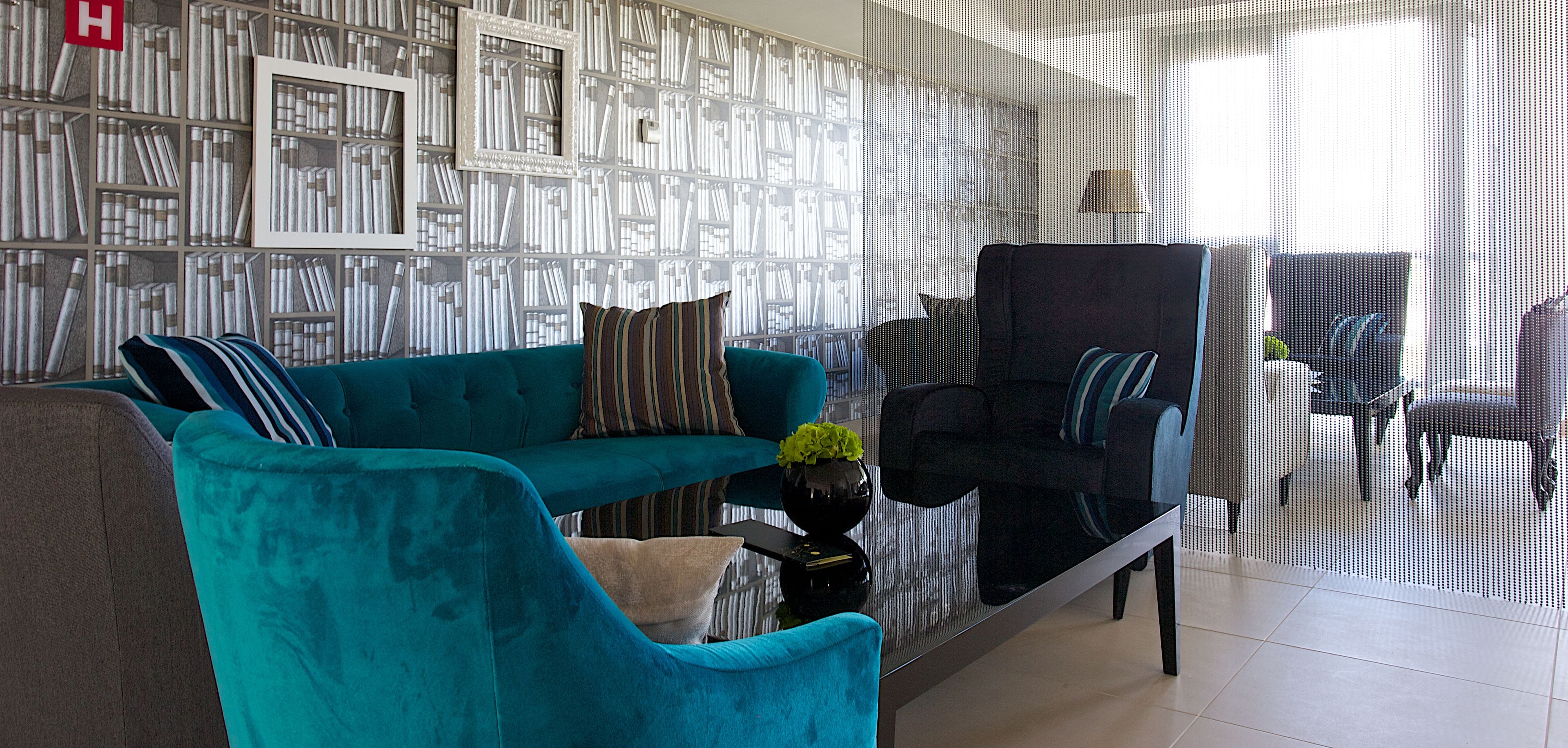 A modern living room with a teal sofa, a black armchair, and a coffee table with a vase.