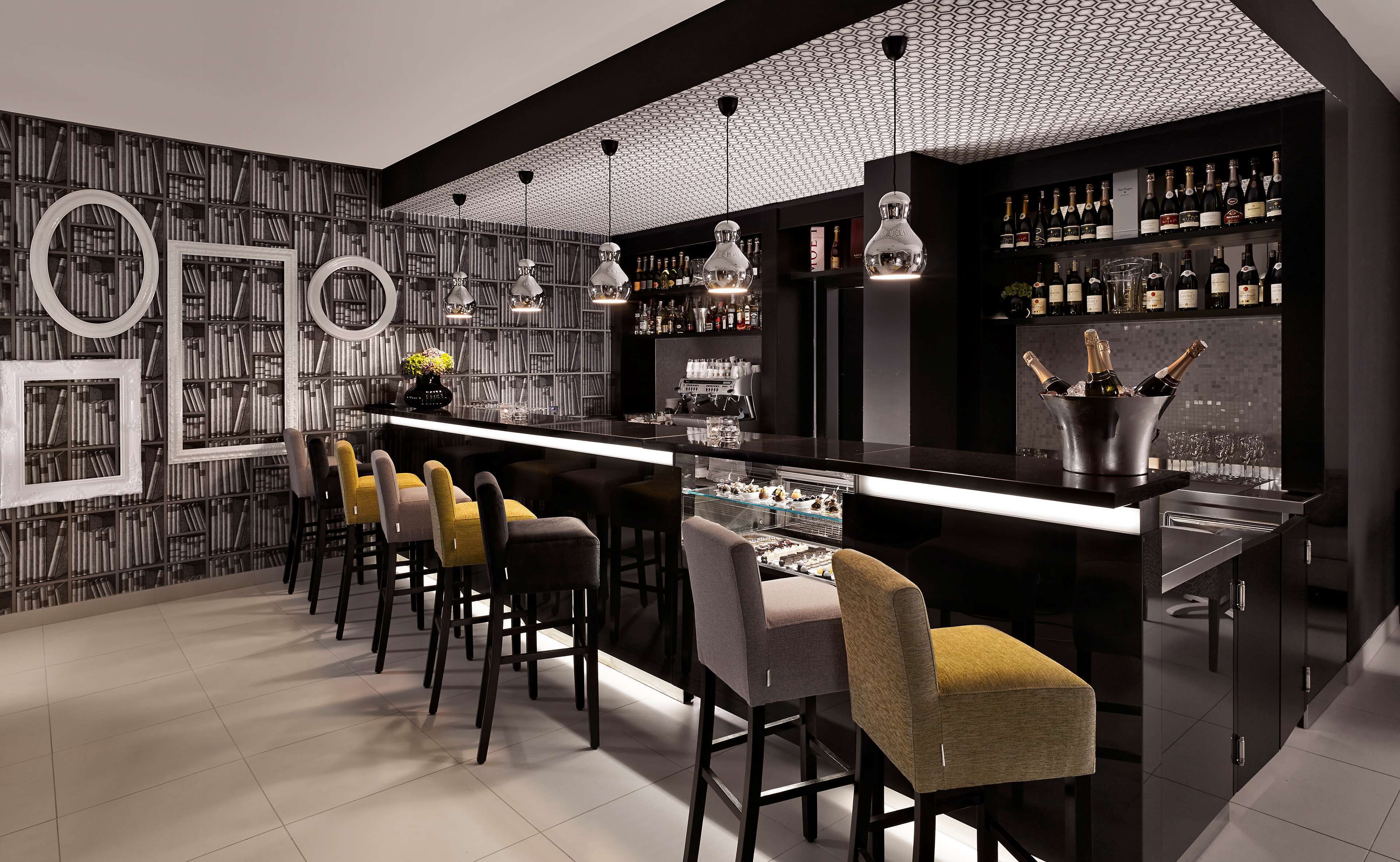 Eine moderne Bar mit langer Theke, mehreren Barhocker, einer Weine- und Spirituosenauslage und einer Wand mit Muster.