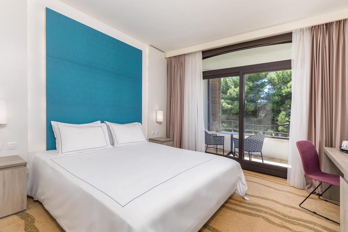 A hotel room with a large bed, a desk, a chair, and a view of the outdoors.