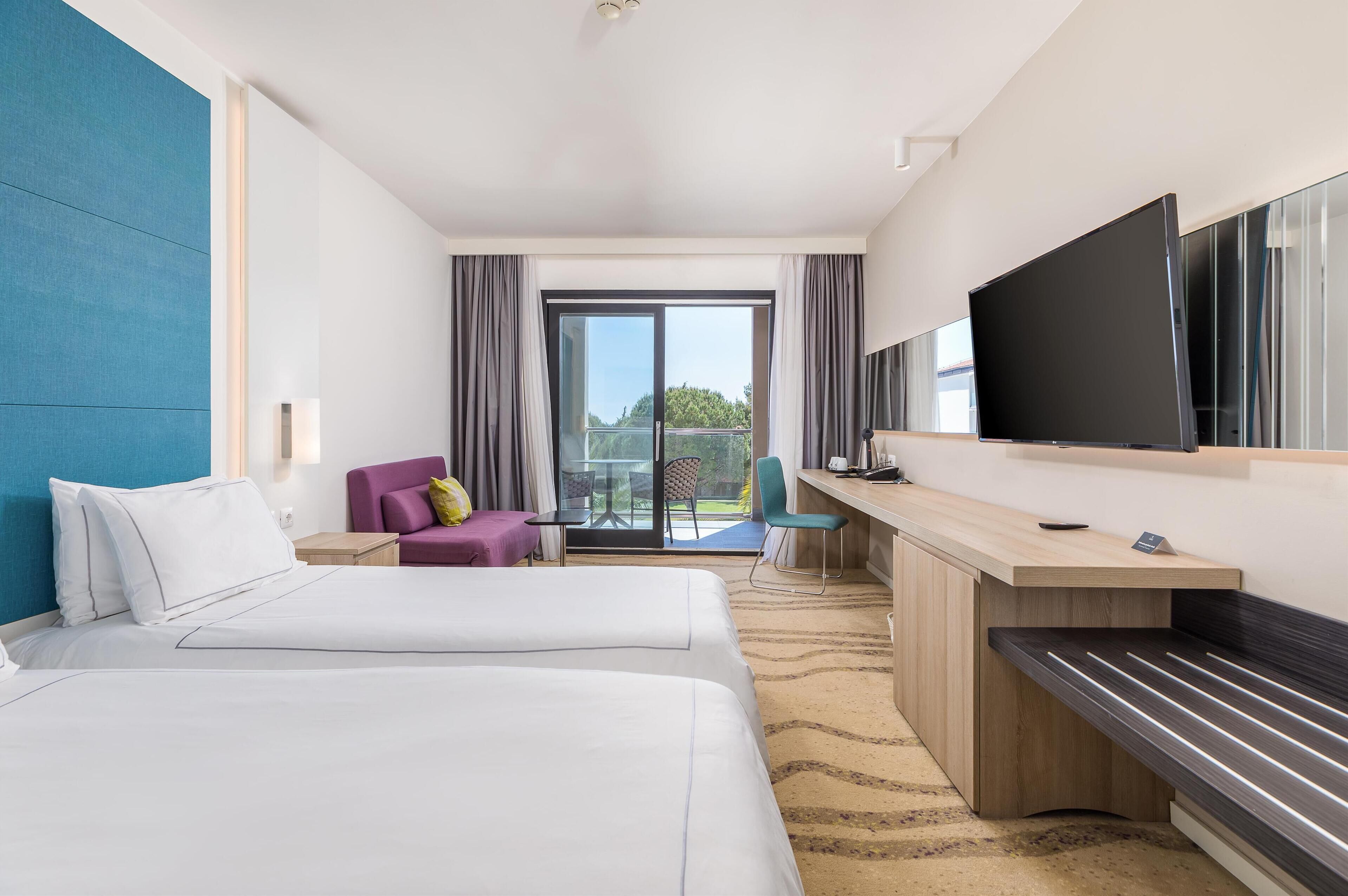 Une chambre d’hôtel avec deux lits, un bureau, une télévision et un balcon avec vue.