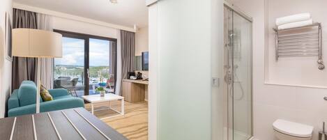 Habitación de hotel con sofá, mesa de comedor, ducha con cerramiento de vidrio y un inodoro.