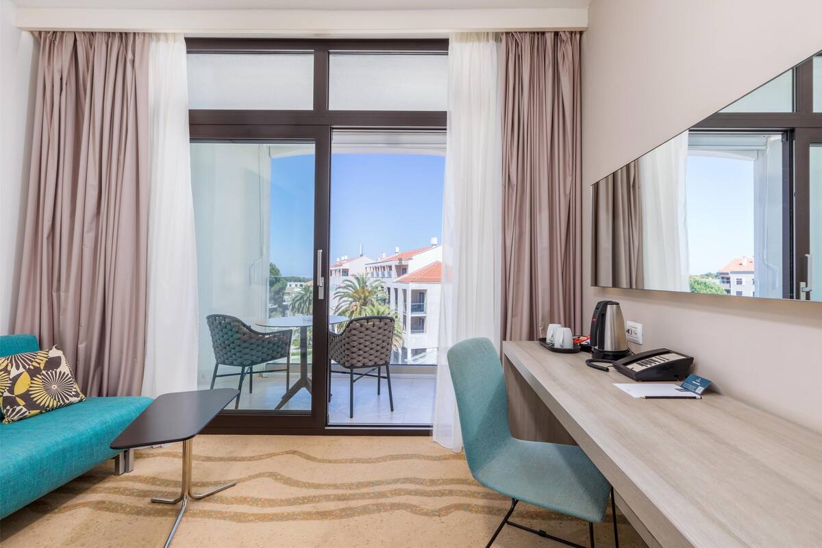 A hotel room with a balcony, a sofa, a desk, and a chair.