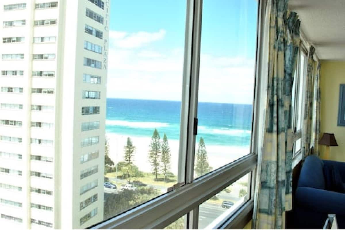 A room with a large window overlooking a beach and tall buildings.