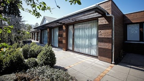 Ein modernes Haus mit Holzfassade, großen Fenstern und einem Kiesweg, der zum Eingang führt.