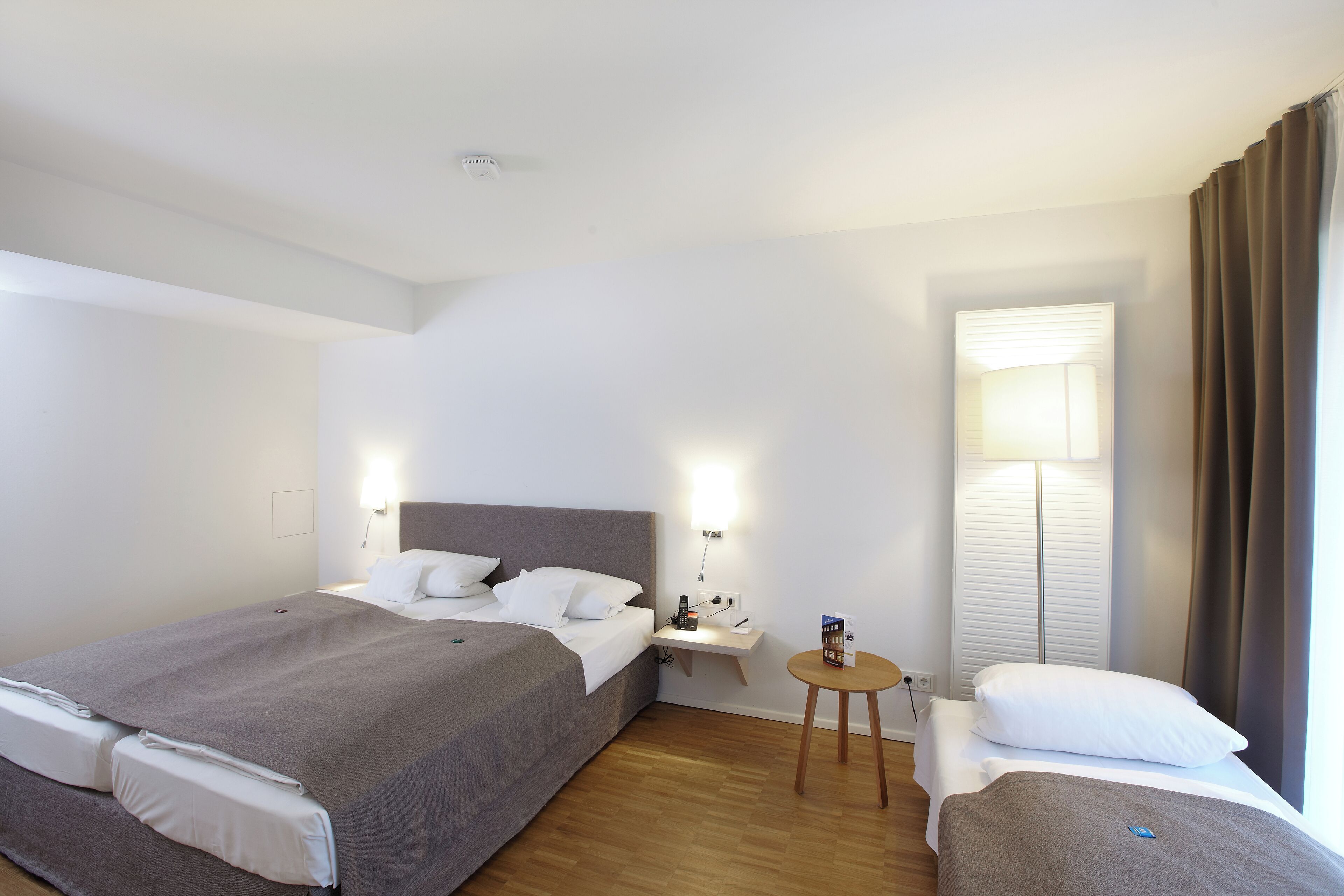 Une chambre d’hôtel avec deux lits, une table de chevet, une lampe et une fenêtre avec des rideaux.