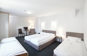 Ein Hotelzimmer mit zwei Betten, einem Schreibtisch mit Stuhl, einem Fernseher und zwei Wandlampen.