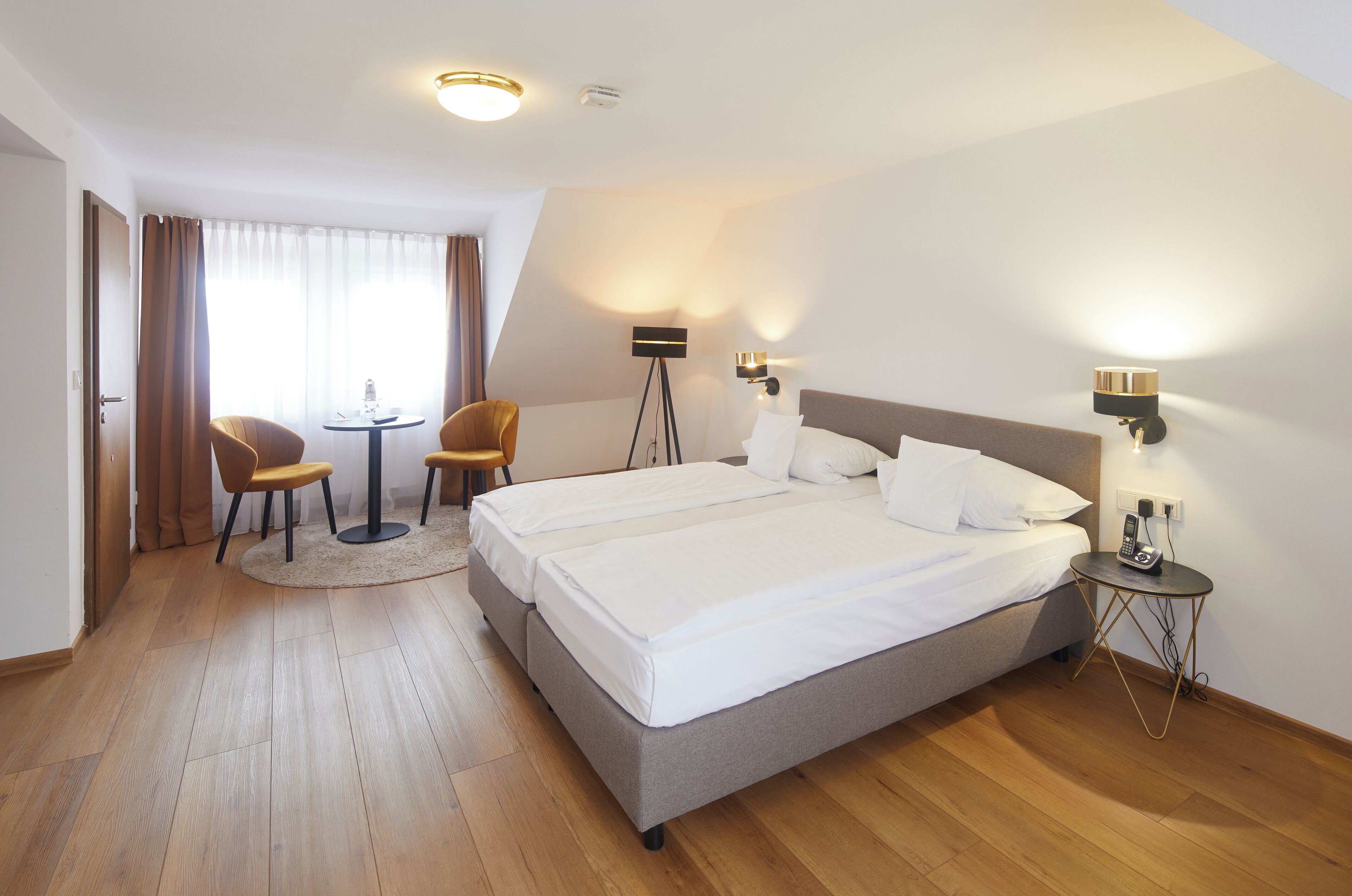 A hotel room with a double bed, two bedside tables, a desk with a chair, a small round table, and a lamp.