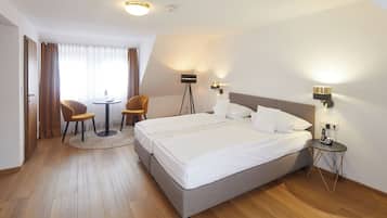 A hotel room with a double bed, two bedside tables, a desk with a chair, a small round table, and a lamp.