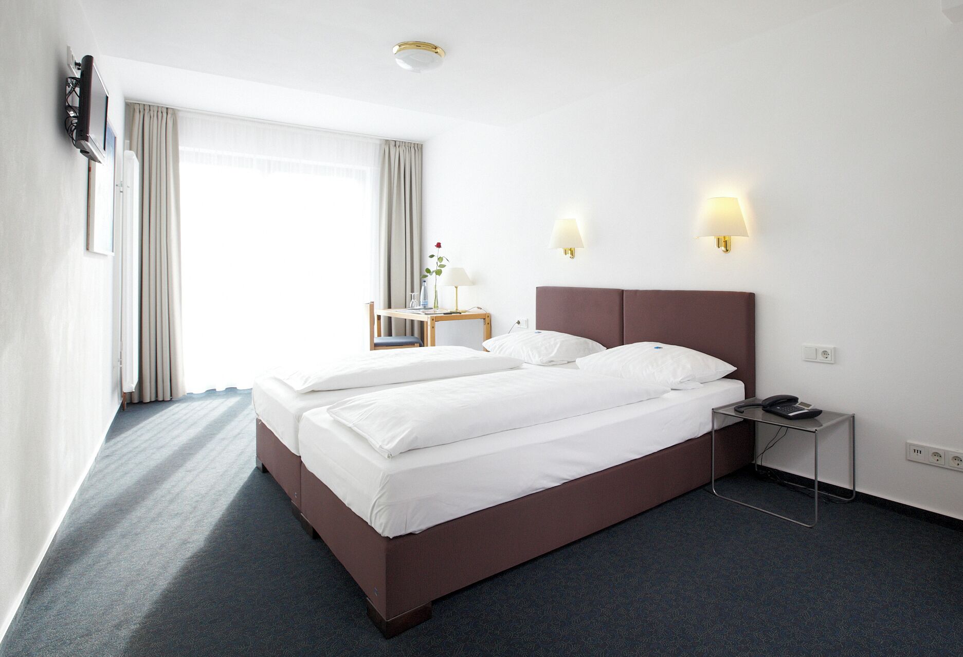 A hotel room with a large bed, bedside tables, a desk, and a lamp.