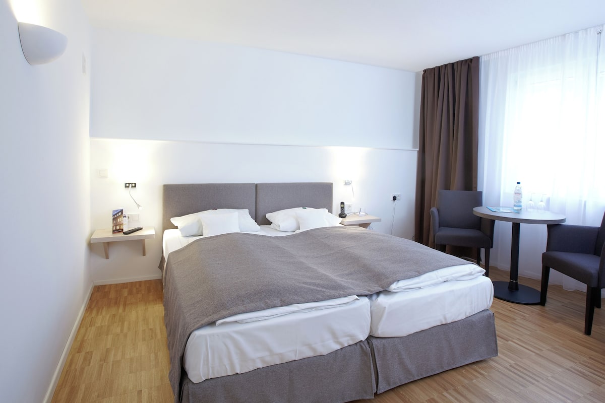 Ein Hotelzimmer mit Bett, Nachttischen, Schreibtisch, Stühlen und einem fenster mit Vorhängen.
