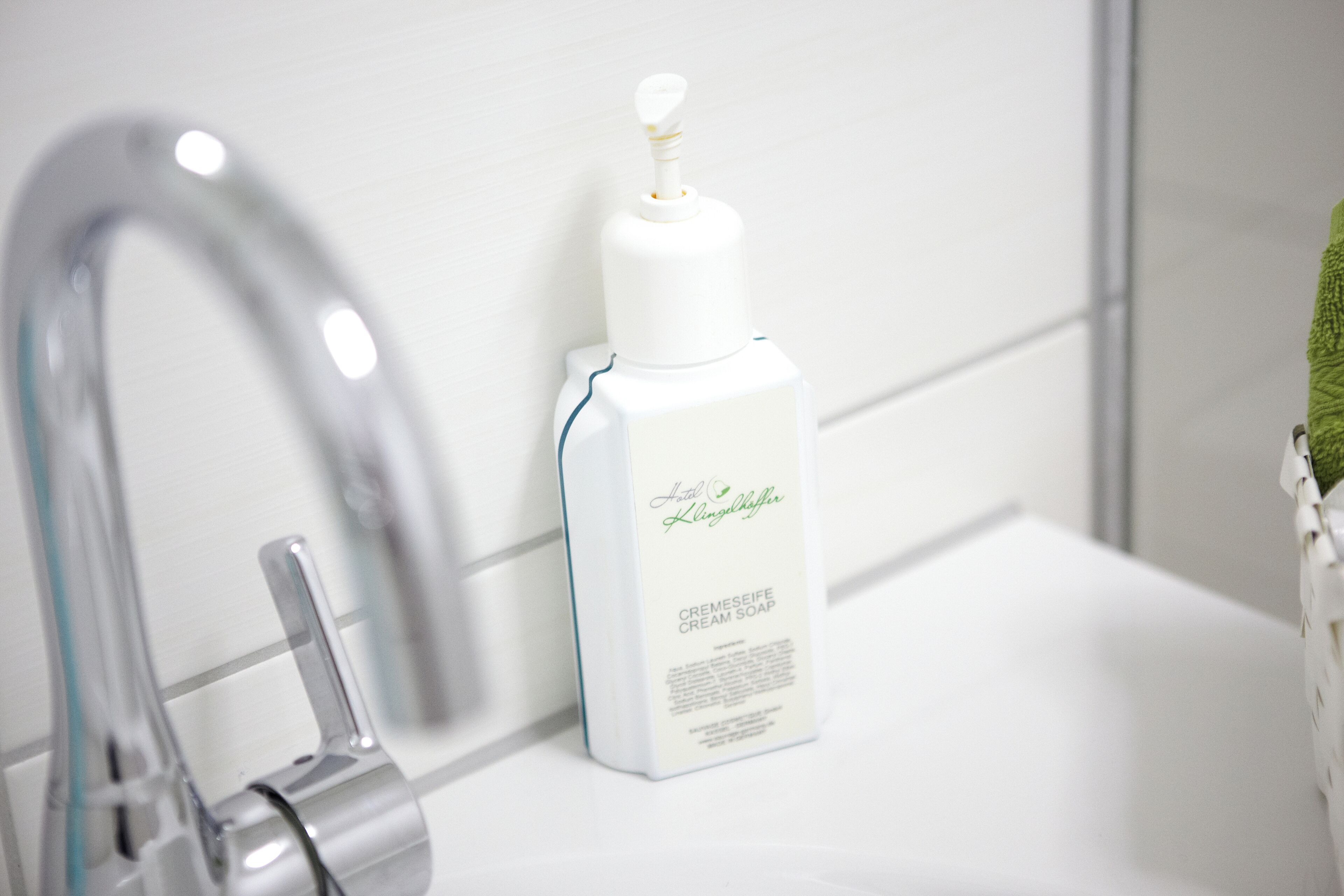 A bathroom with a white sink, a silver faucet, and a bottle of cream soap.