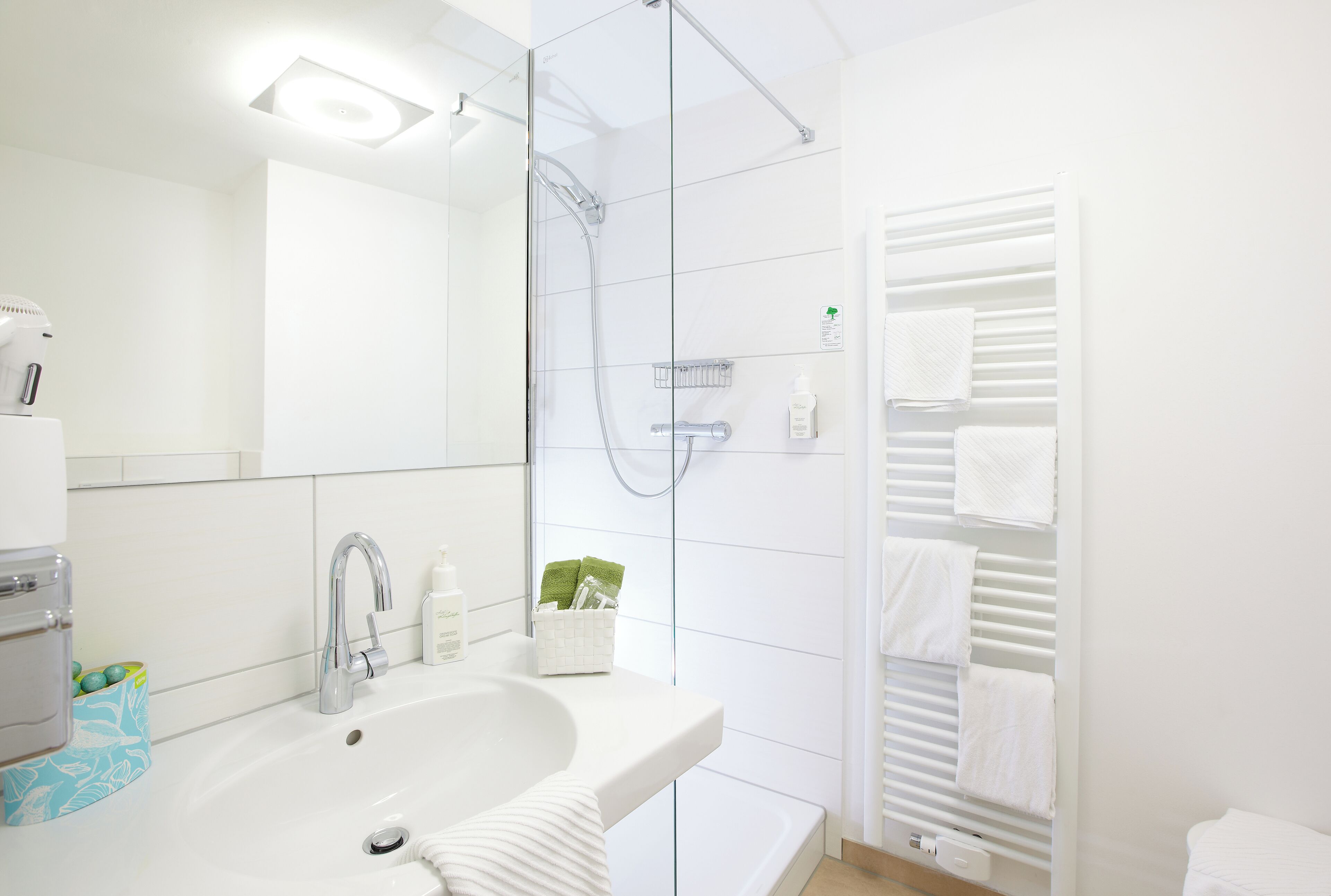 Un baño moderno con lavabo, espejo, ducha y tendedero para toallas.