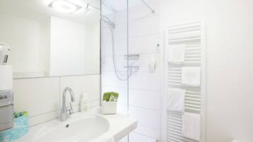Un baño moderno con lavabo, espejo, ducha y tendedero para toallas.