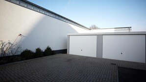 Ein modernes Gebäude mit flachem Dach, zwei großen weißen Garagentoren und einem gepflasterten Innenhof mit Ziegelmuster.