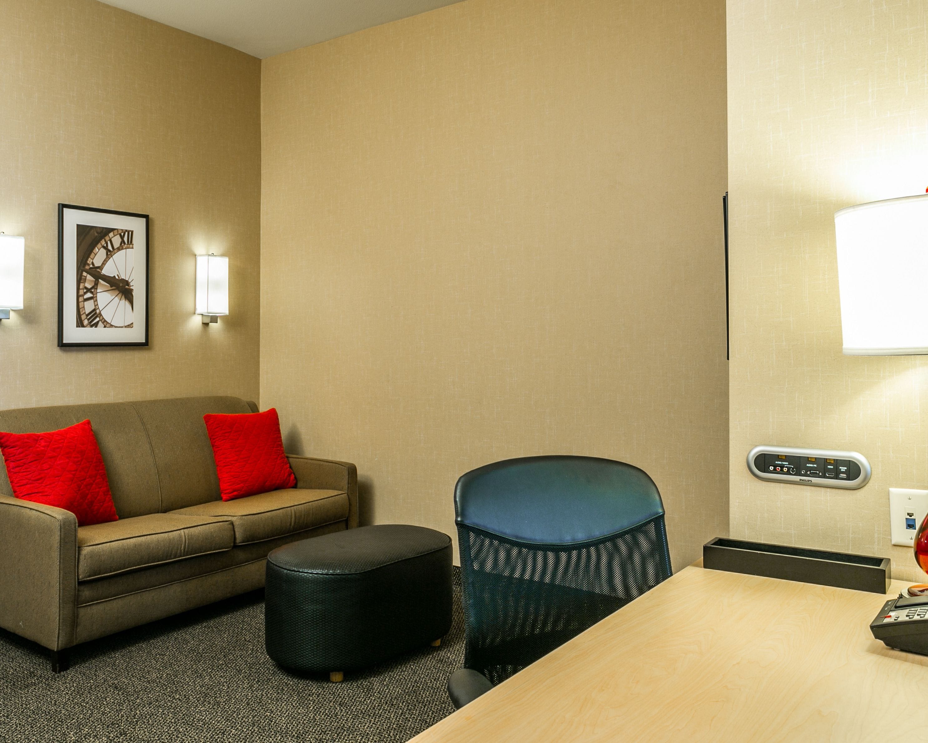 A hotel room with a sofa, ottoman, and a table with a remote control.