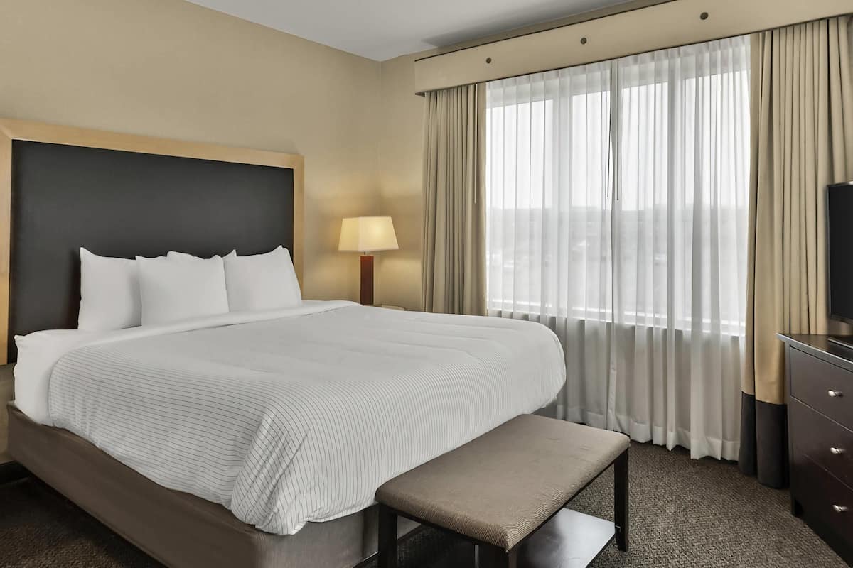 Ein Hotelzimmer mit einem großen Bett, einem Nachttisch, einer Lampe, einer Bank und einem Fernseher.