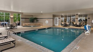 An indoor swimming pool with clear water, surrounded by lounge chairs and tables, and a stone wall with a door. - Cambria Hotel Columbus - Polaris (Columbus)