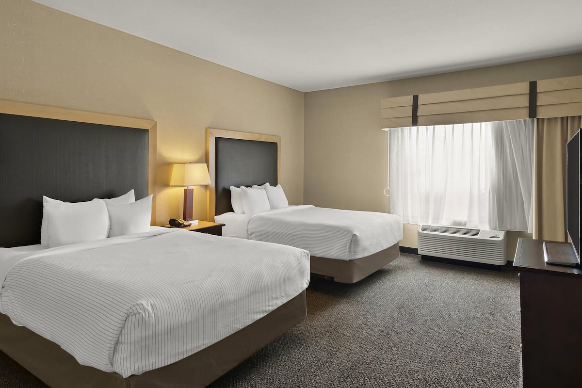 Ein Hotelzimmer mit zwei Betten, einem Schreibtisch, einer Lampe und einer Klimaanlage.