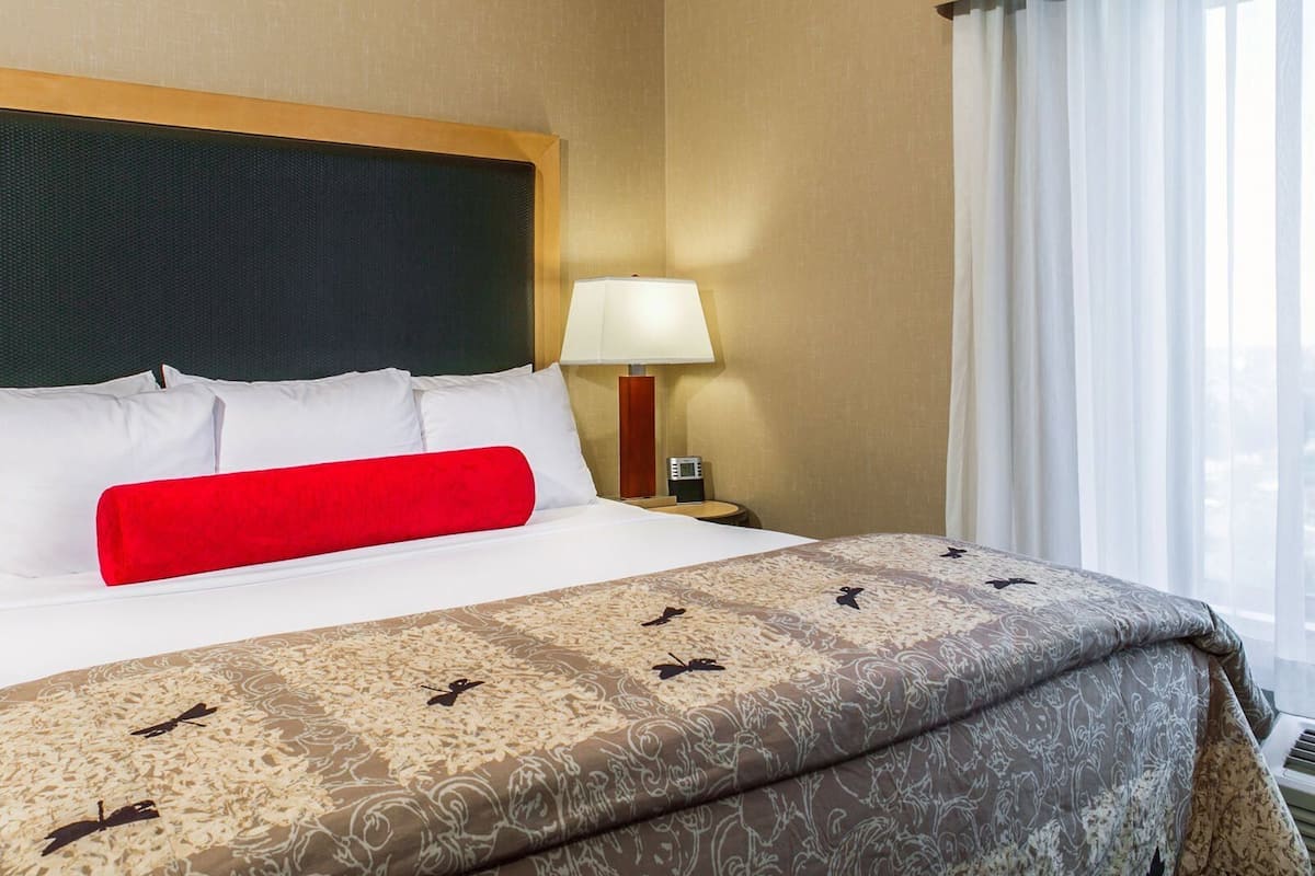 Ein Hotelzimmer mit Bett, Nachttisch, Lampe und einem Vorhangfenster.