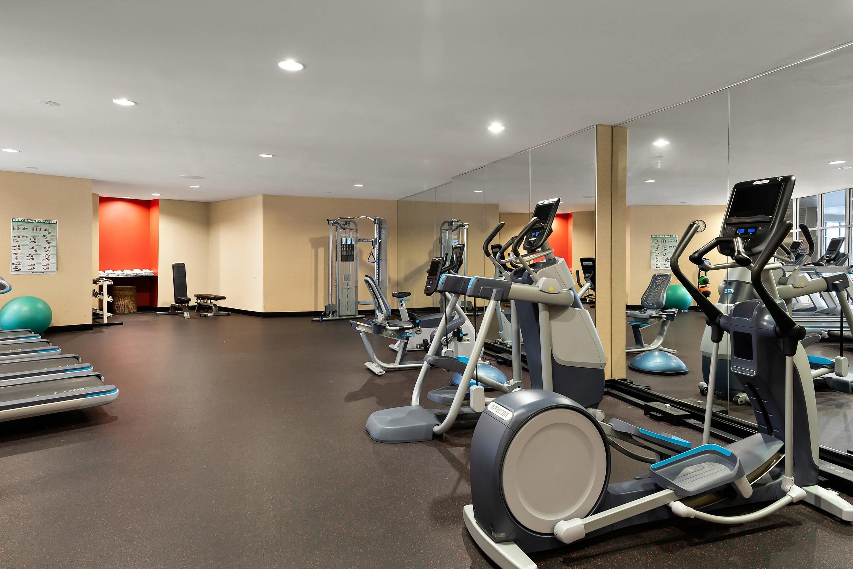A gym with treadmills, elliptical machines, and exercise balls.