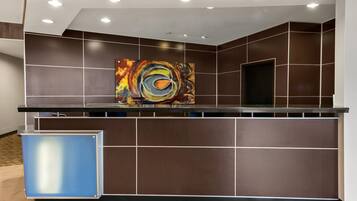 A reception area with a modern design, featuring a large abstract painting, a reception desk, and a blue information kiosk.