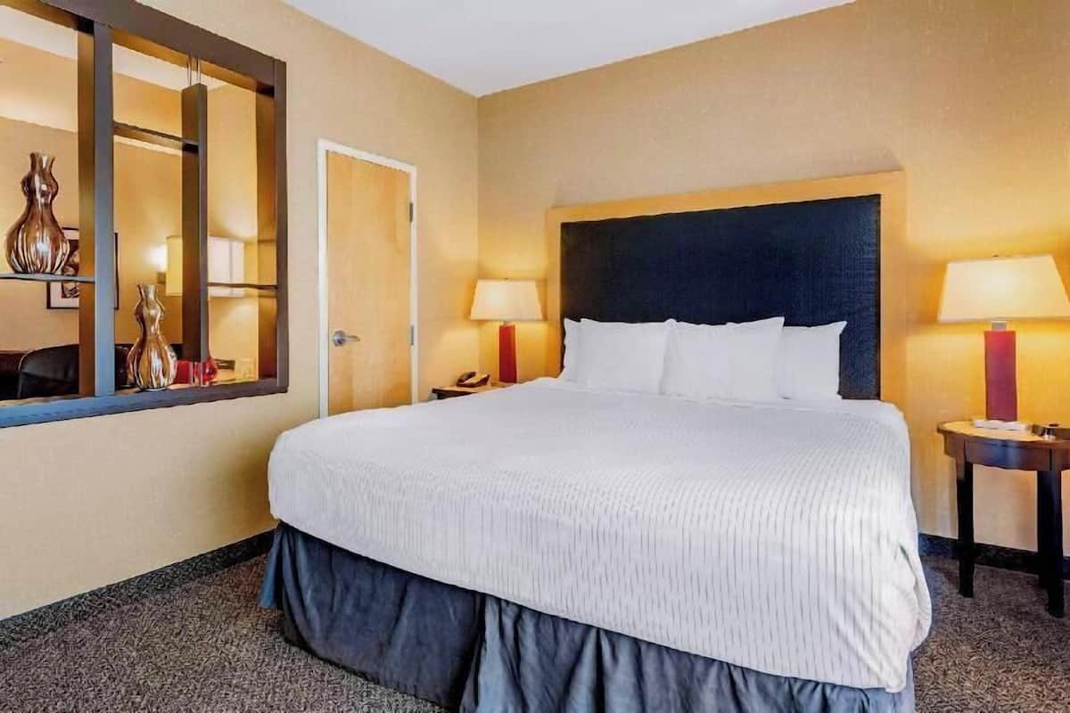 Ein Hotelzimmer mit einem großen Bett, zwei Nachttischen inklusive Lampen, einem Spiegel und einer Tür.