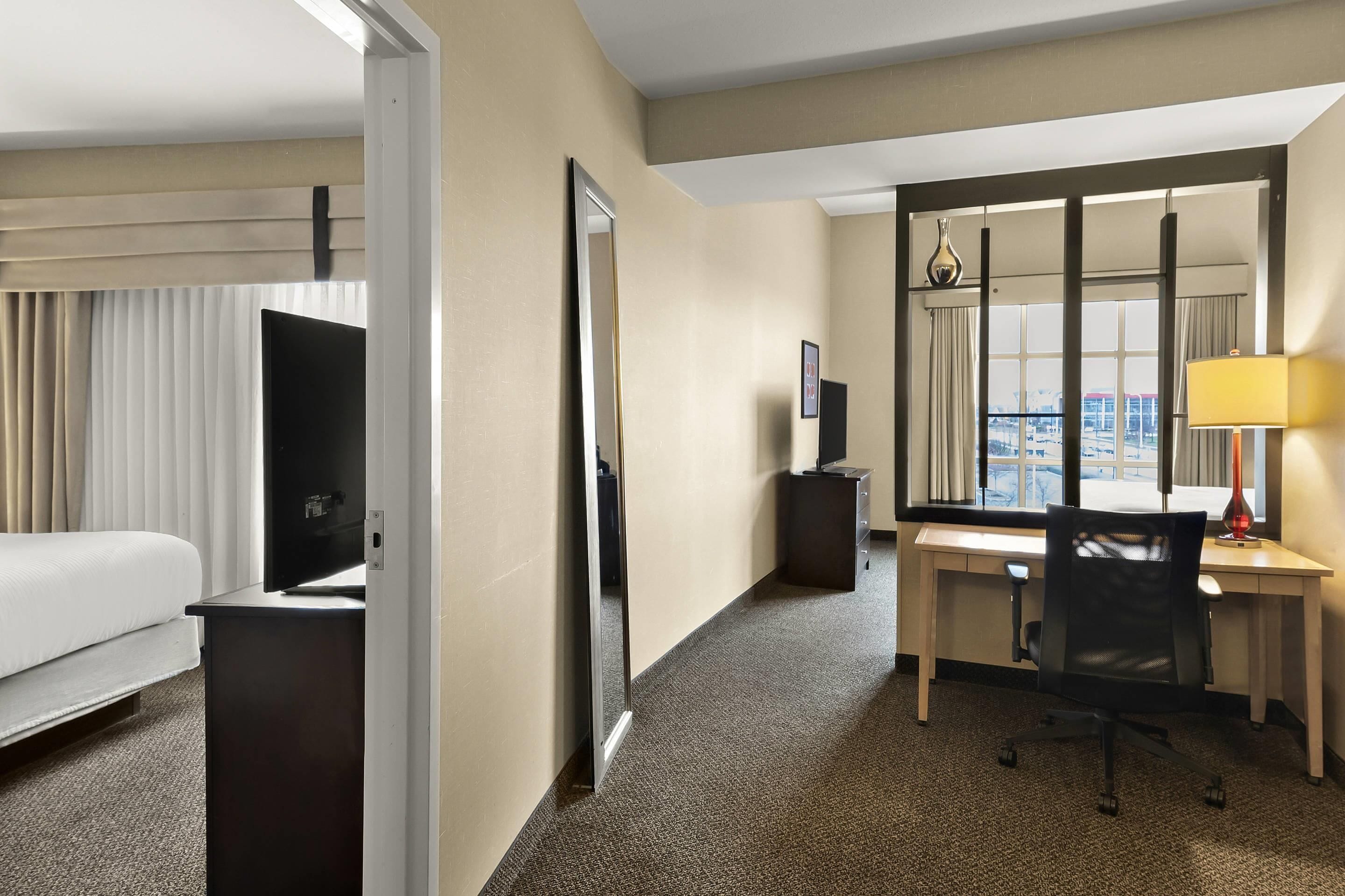 A hotel room with a bed, a desk, a chair, a TV, a mirror, and a window with a view.
