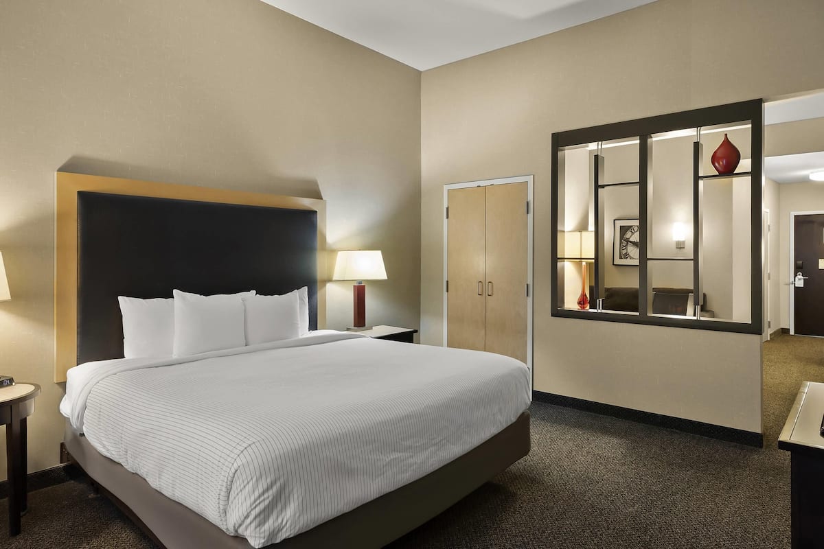 Ein Hotelzimmer mit einem großen Bett, einem Nachttisch mit Lampe, einem Schrank und einem Spiegel mit dekorativer Vase.