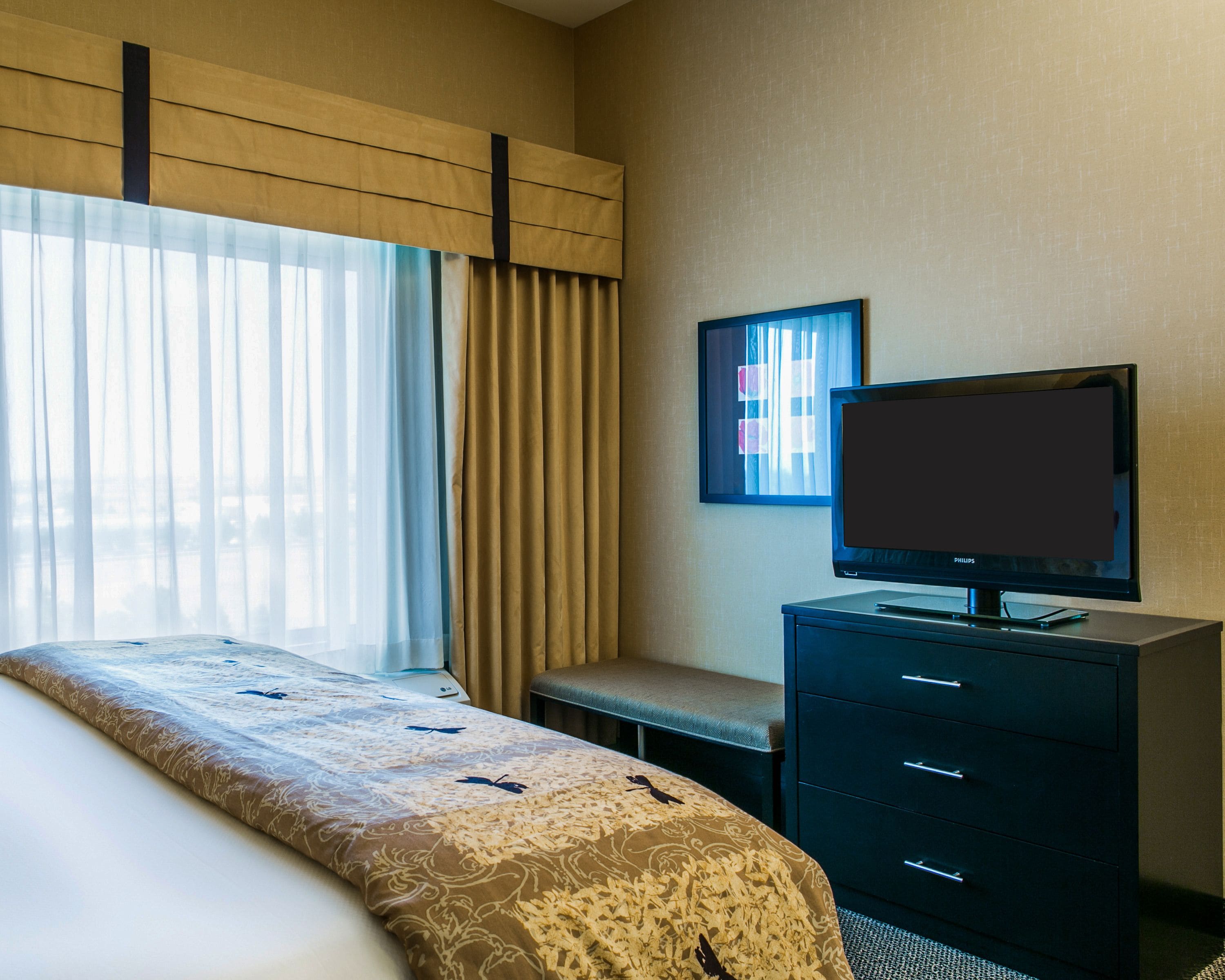 Una habitación de hotel con una cama, un televisor en una cómoda y una ventana con cortinas.