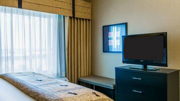 Una habitación de hotel con una cama, un televisor en una cómoda y una ventana con cortinas.