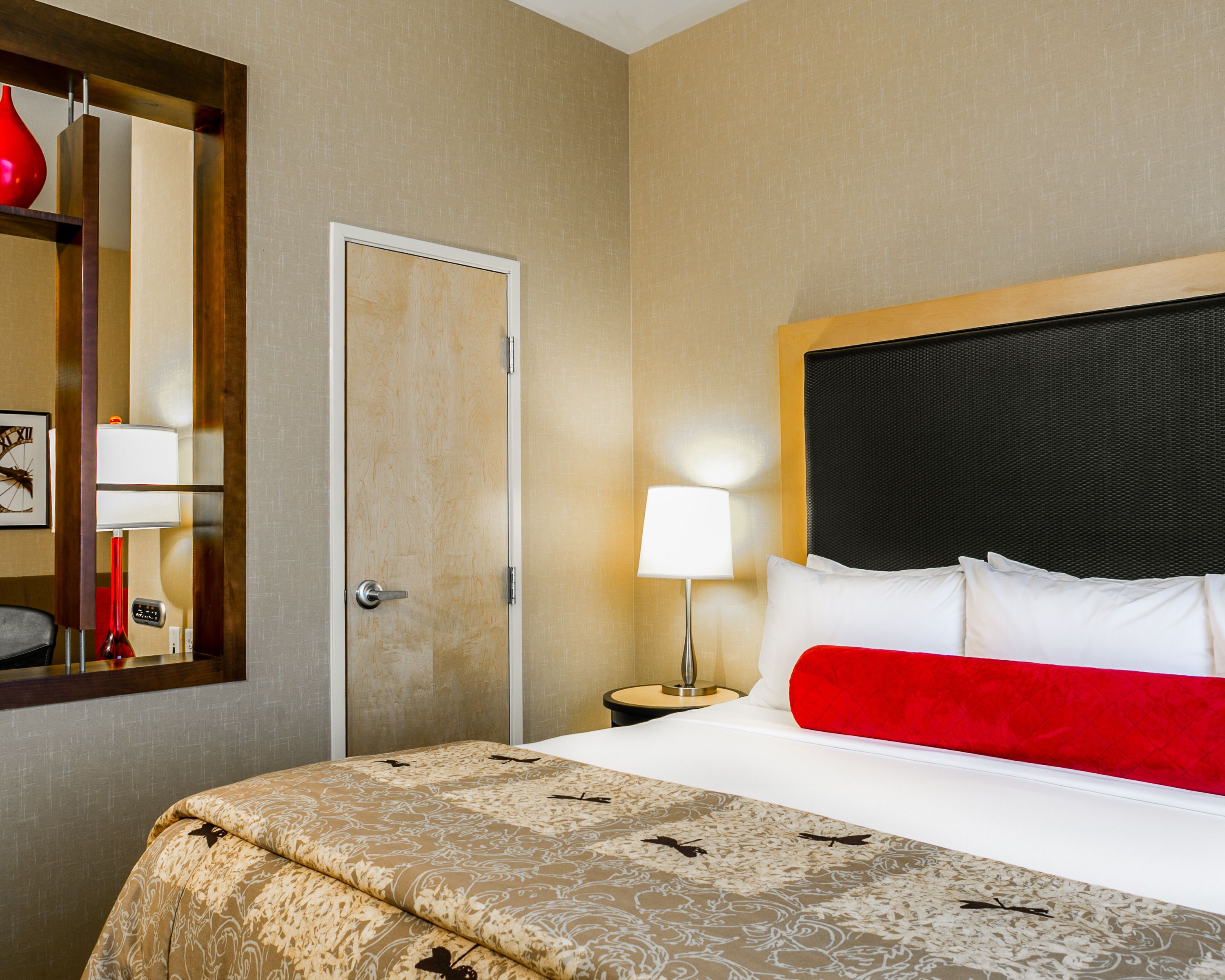 A hotel room with a bed, a nightstand, a lamp, and a door.