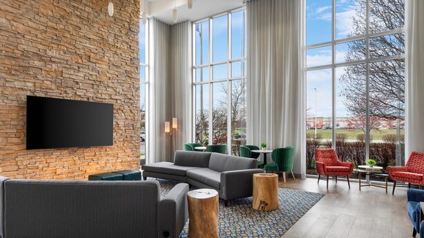 A modern lounge area with a brick wall, large windows, and a flat-screen TV. - Cambria Hotel Columbus - Polaris (Columbus)