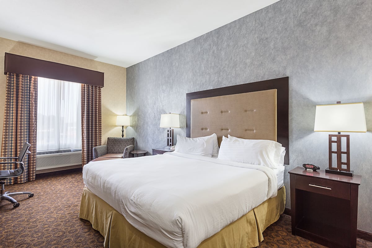 Une chambre d’hôtel avec un grand lit, un bureau, une chaise et une fenêtre avec des rideaux.