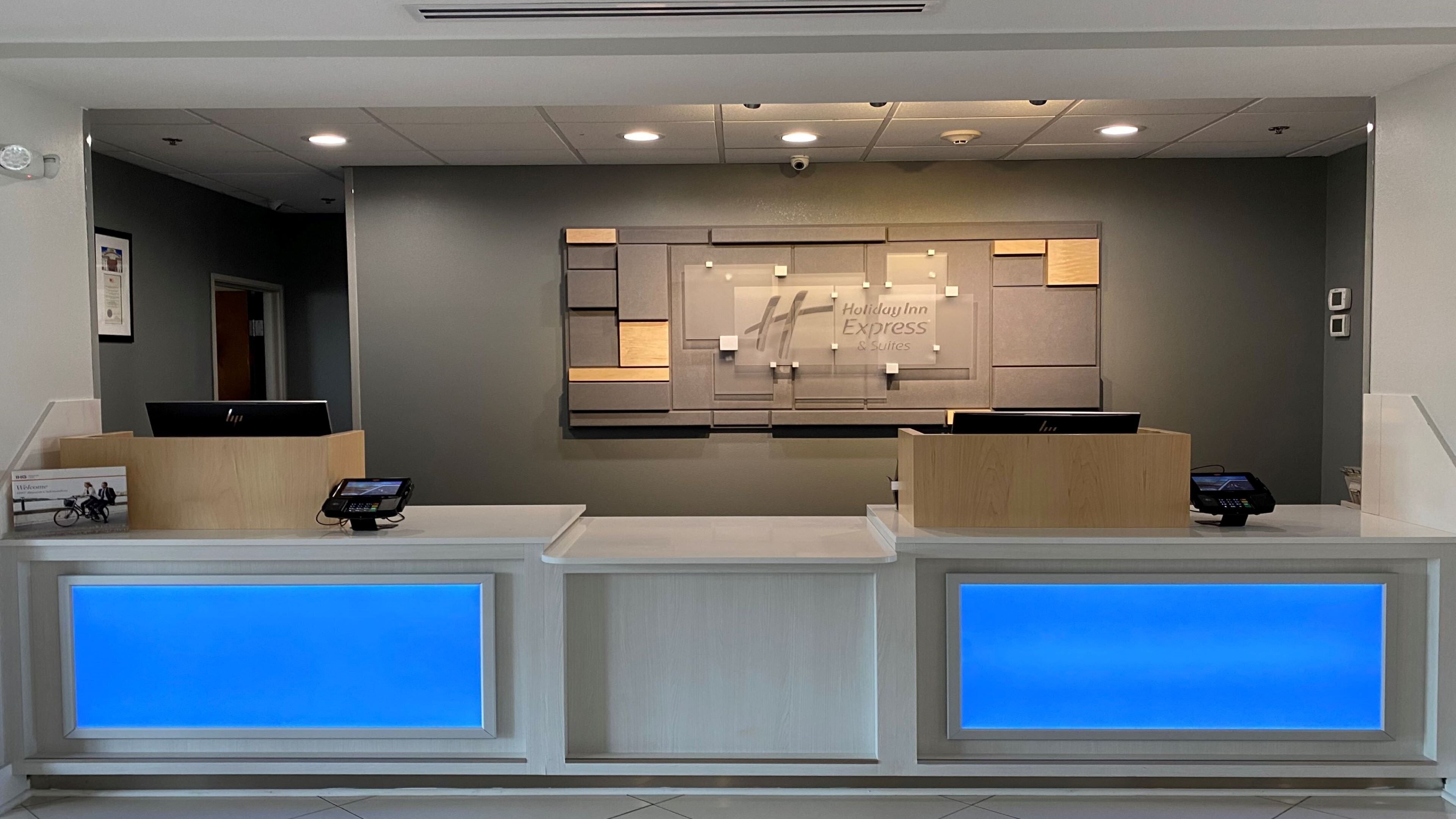 A hotel reception desk with two computer stations, a wall-mounted sign, and a blue-lit window.