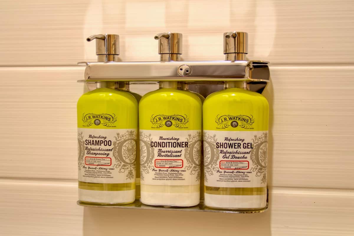 Un distributeur mural pour la salle de bain contenant trois flacons de produits J.R. Watkins : shampoing, après-shampoing et gel douche.