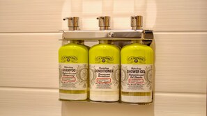 A bathroom wall-mounted dispenser with three bottles of J.R. Watkins products: shampoo, conditioner, and shower gel. - Holiday Inn Express Hotel & Suites BYRAM by IHG (Byram)