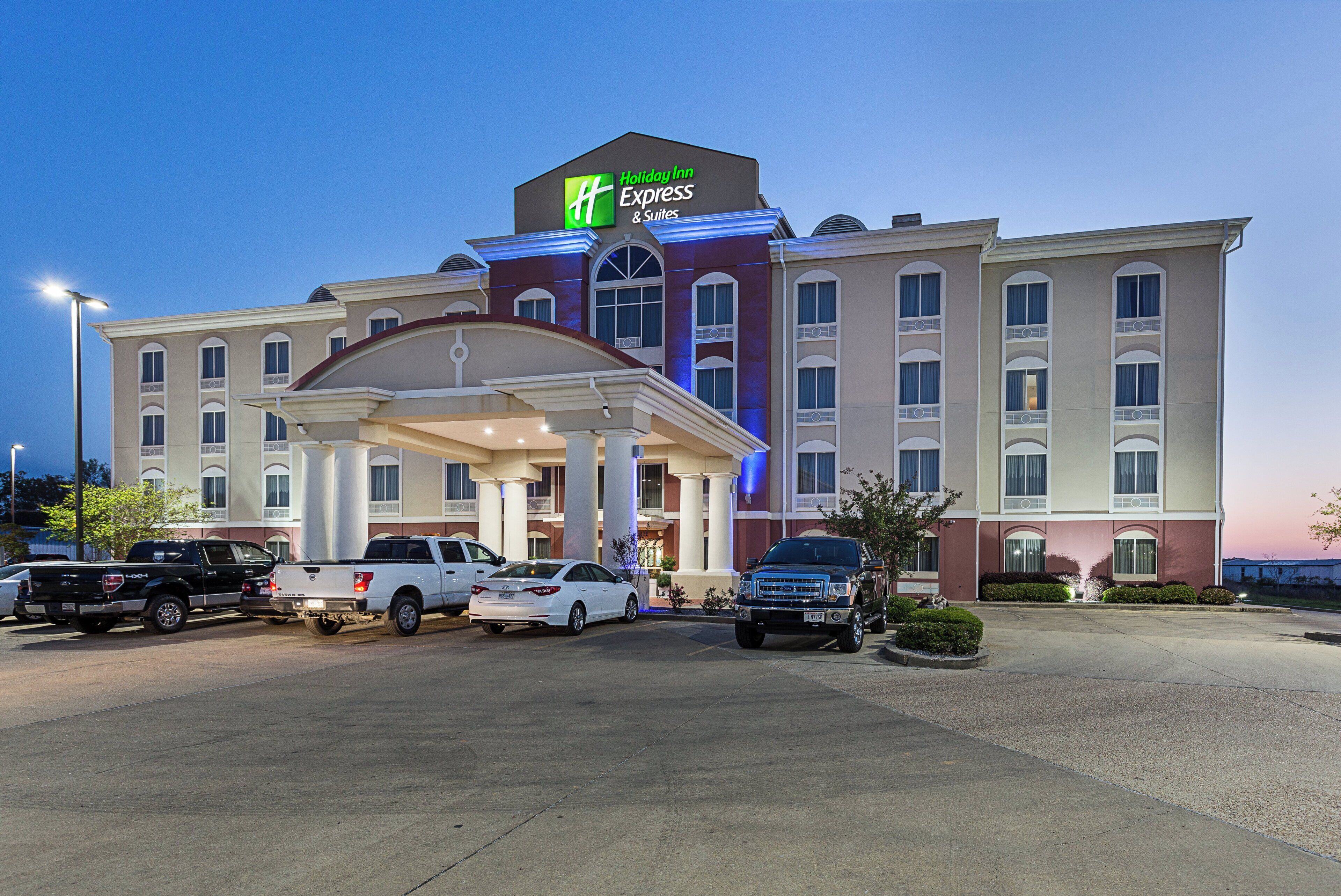 Ein Holiday Inn Express & Suites Hotel mit überdachter Eingangspartie, mehreren Parkplätzen und einer gut beleuchteten Fassade.