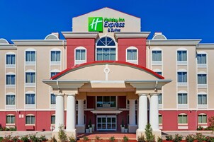 Un hotel Holiday Inn Express & Suites con una fachada simétrica, un amplio acceso con marquesina y un cielo azul despejado.