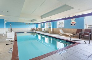 An indoor swimming pool with clear water, a lifeguard chair, lounge chairs, and a pool rules sign.