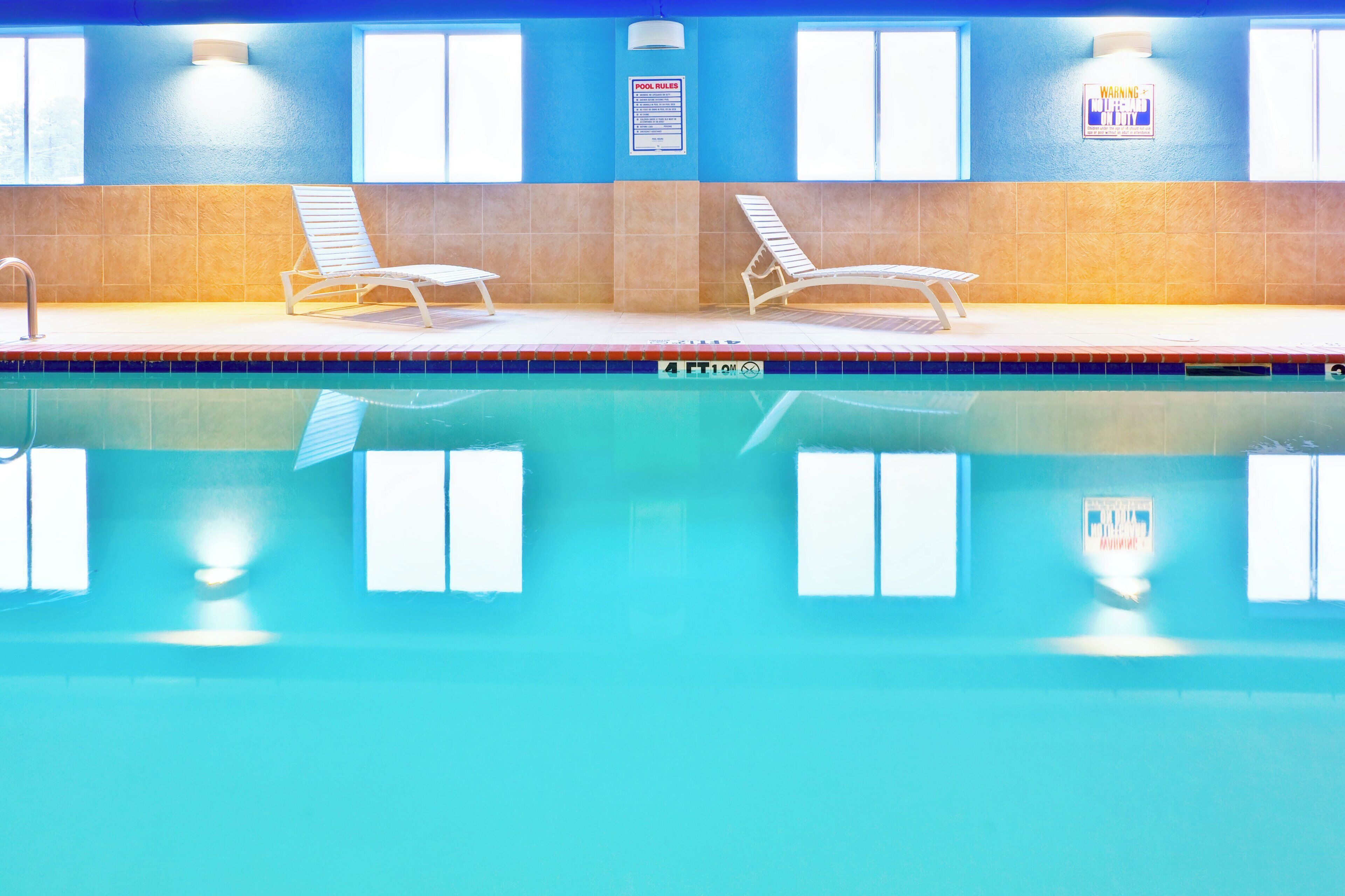 A swimming pool with two sun loungers, a pool rule sign, and a warning sign on the wall.