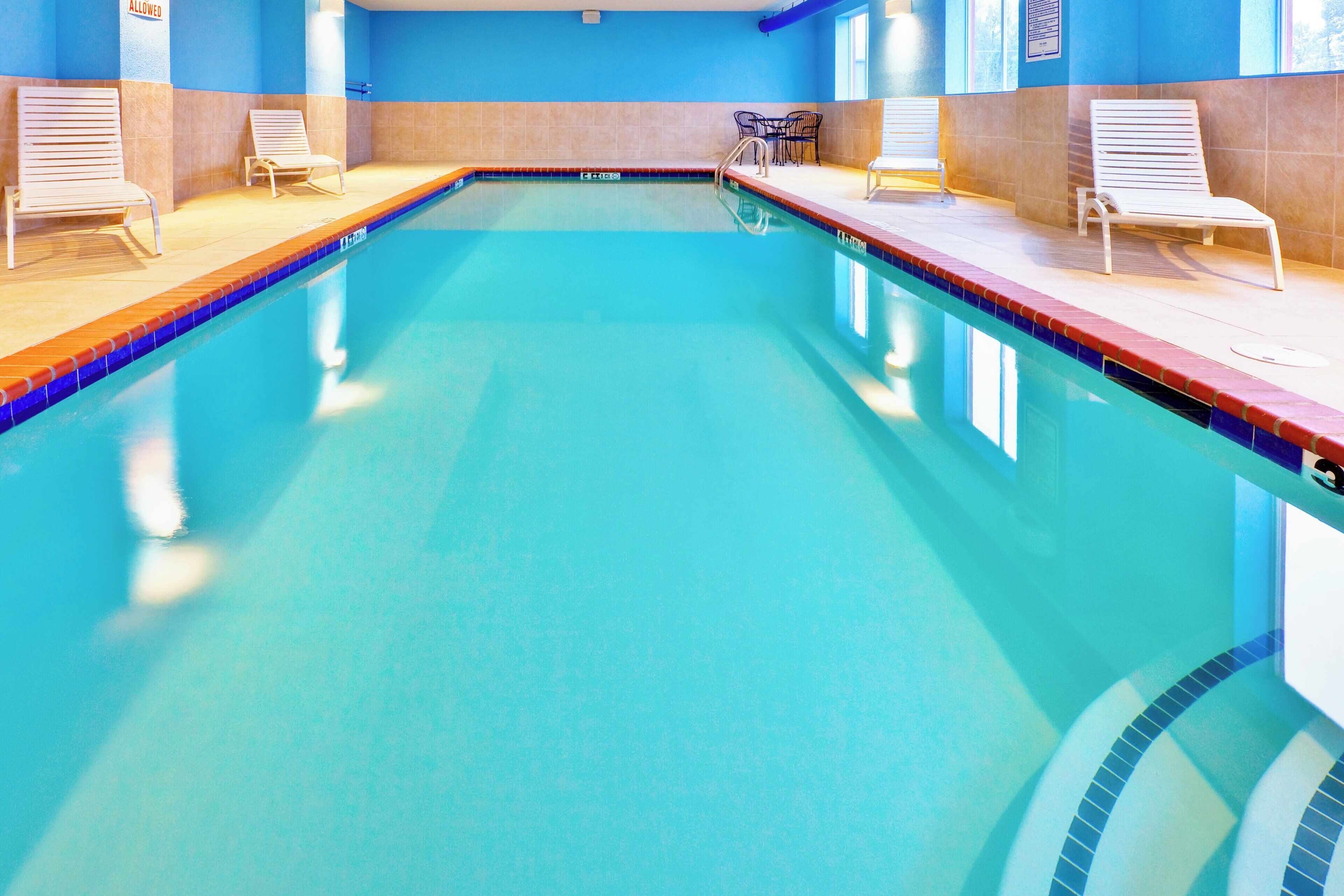 An indoor swimming pool with clear water, surrounded by lounge chairs and a tiled floor.
