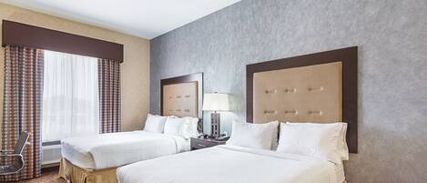 Ein Hotelzimmer mit zwei Betten, einem Schreibtisch mit Lampe, einem Stuhl und einem großen Fenster mit Vorhängen.