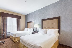 Habitación de hotel con dos camas, un escritorio con lámpara, una silla y un ventanal con cortinas.