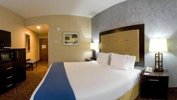 Habitación de hotel con una cama grande, un escritorio con lámpara, televisor y microondas.
