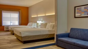 A hotel room with two beds, a blue sofa, a large window, and a wall-mounted artwork.