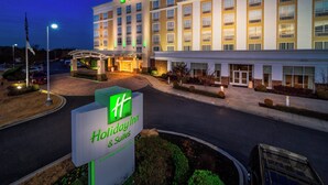 Un hotel Holiday Inn & Suites con un letrero grande, varios pisos y una entrada bien iluminada.